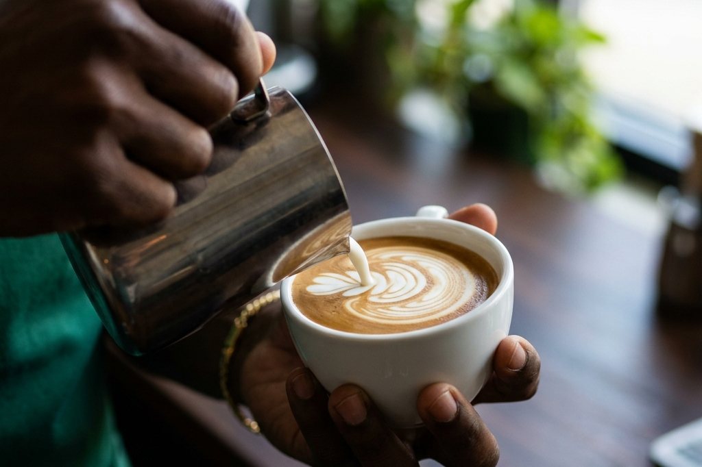 A barista pouring latte art into a white cup